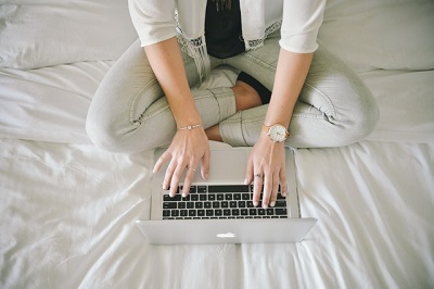 A female on her laptop while sat on a bed